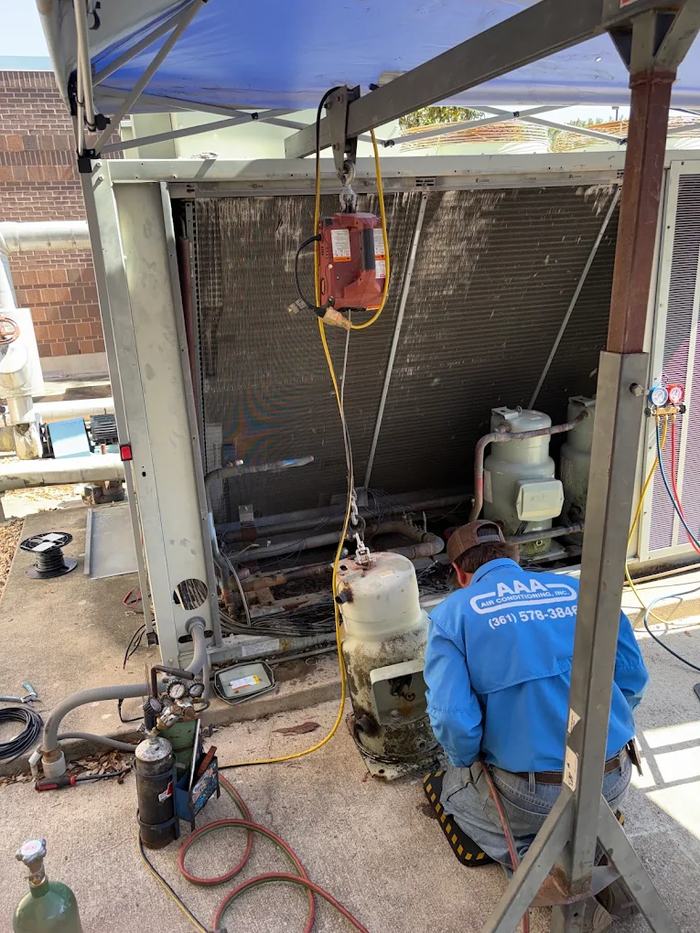 Technician replacing a compressor inside a commercial HVAC unit under a shade canopy