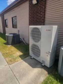 Ductless mini split heat pump outdoor unit installed beside a residential condenser