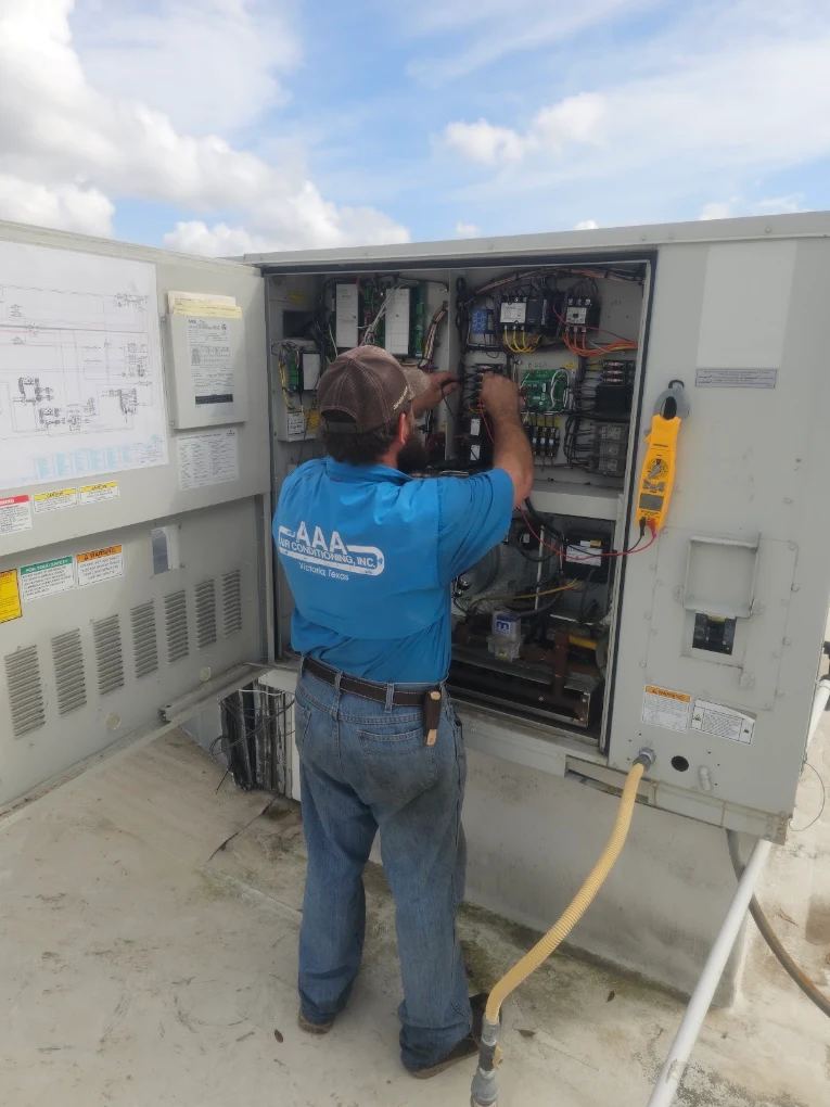 AAA Air Conditioning technician troubleshooting the control panel of a rooftop HVAC unit in Victoria, Texas
